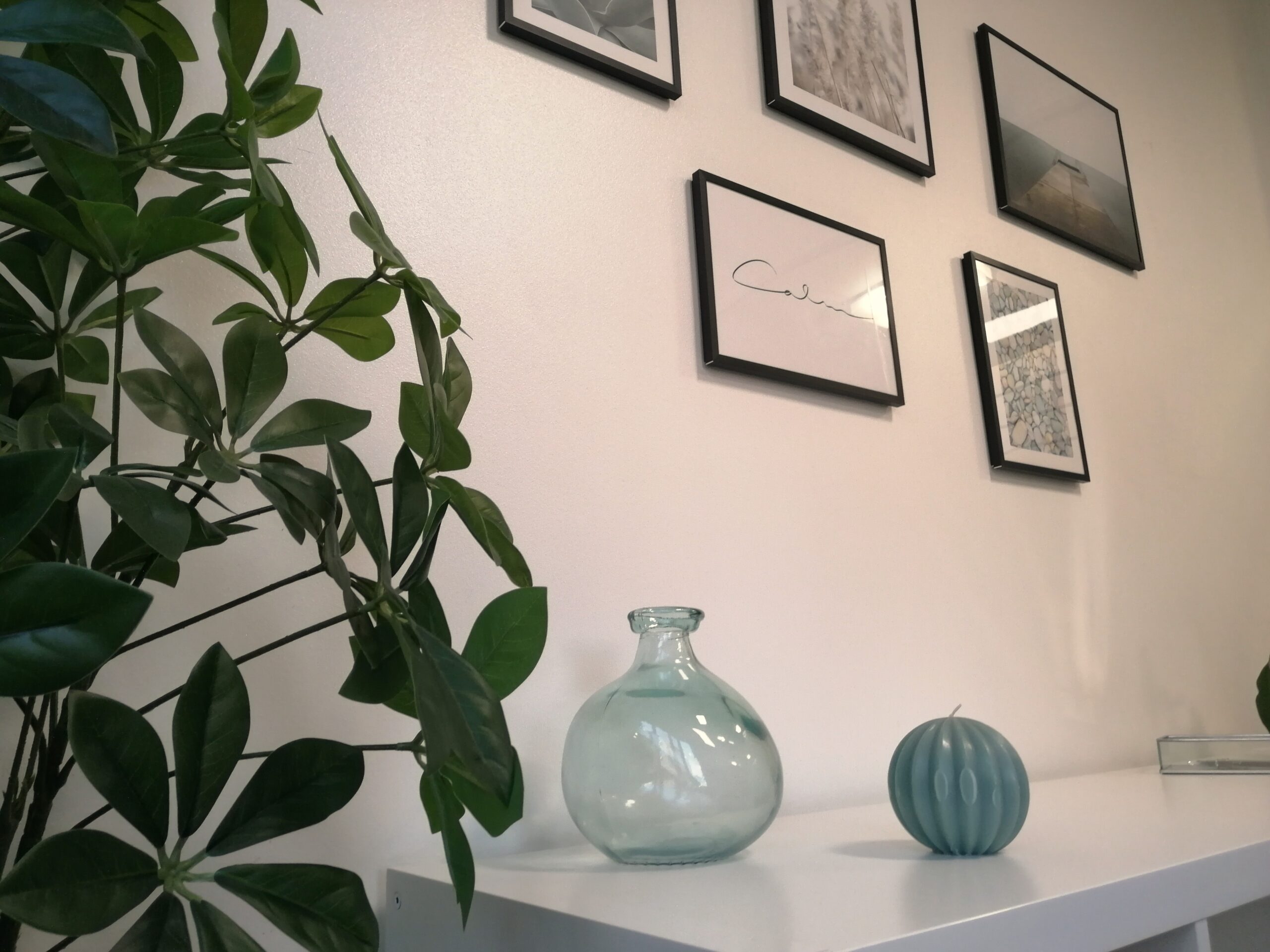 Decoración minimalista en consulta de psicología con planta, jarrón de cristal y cuadros en la pared